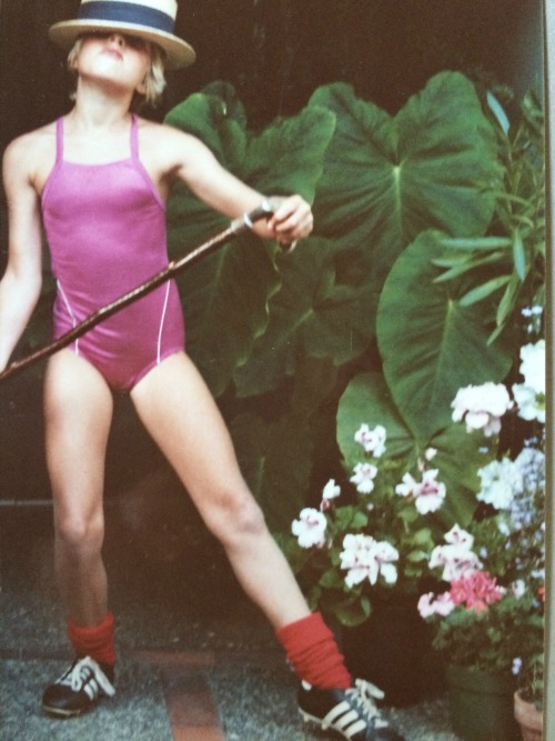 A young Erica Hargreave of around 8 -10, performing a dance in a straw flat top hat tilted down over her eyes, with a cane, while dressed in a purple swimsuit and wearing soccer cleats.