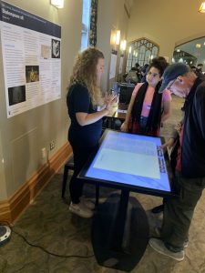 Project Lead Olivia How, demonstrating Shakespeare xR's touch table of Shakespeare’s First Folio to interested onlookers.